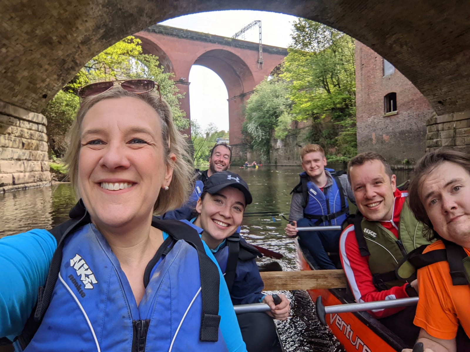 A team of 6 from Stockport Council take a selfie on the charity canoe challenge underneath Stockport's viaduct; their paddles in hand as they canoe on the River Mersey