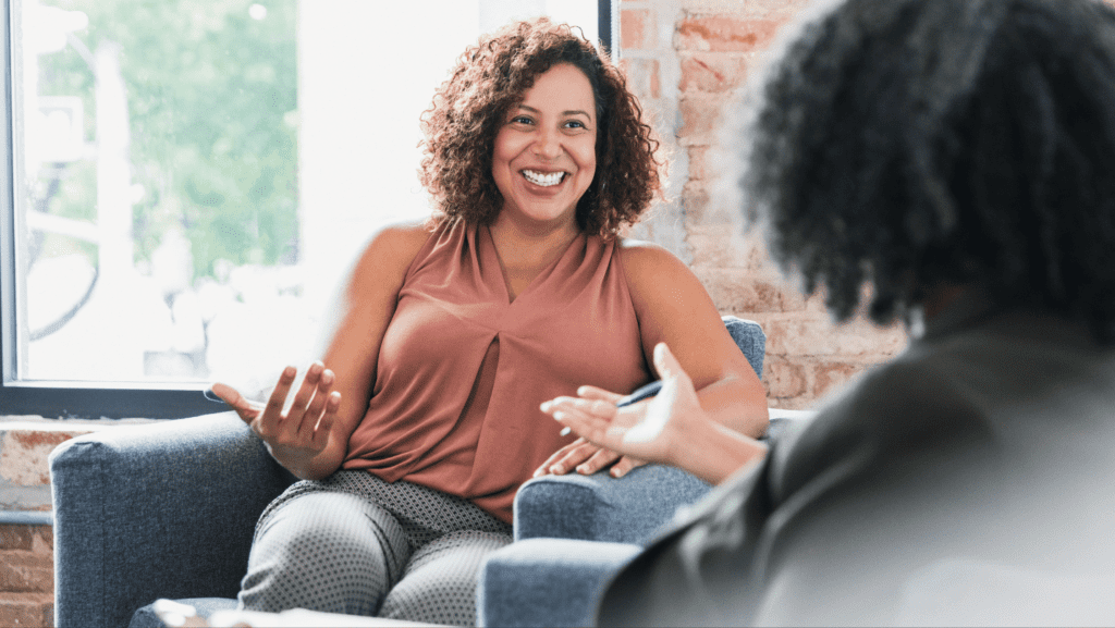 A client is sat on a chair smiling at a counsellor sat across from them